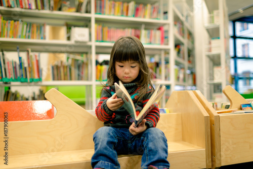 little girl reading a book in a library
