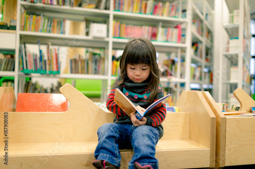 little girl reading a book in a library