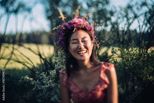 Happy young woman in a wreath from wildflowers and grass. Cute girl with summer flowers, closeup