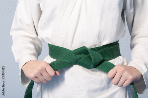 Hands tightening green belt on a teenage dressed in kimono for martial arts photo