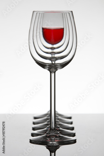 Row of empty wine glassesand one filled at the rear standing on reflective surface photo