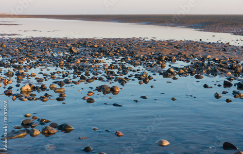 Beautiful sunny winters day on a british beach, with sand ripples, beach stones and the sky reflecting in a water pool.