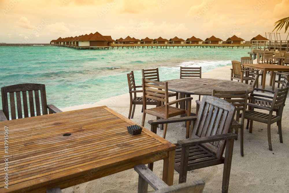 wooden tables and chairs in restaurant on Maldives island with sunset view point