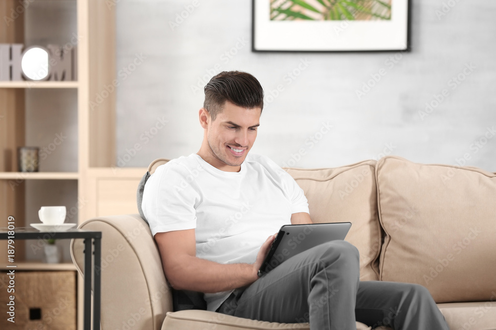 Handsome man using tablet pc while resting on sofa at home