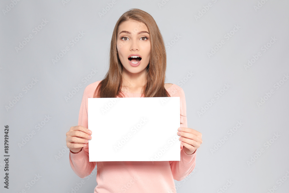 Emotional young woman with blank sheet of paper on grey background Emotional young woman with blank sheet of paper on grey background