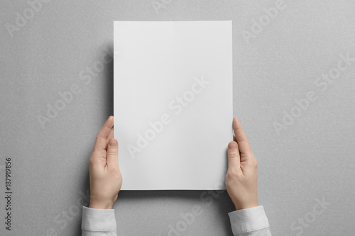 Woman holding blank sheet of paper on light background. Mock up for design