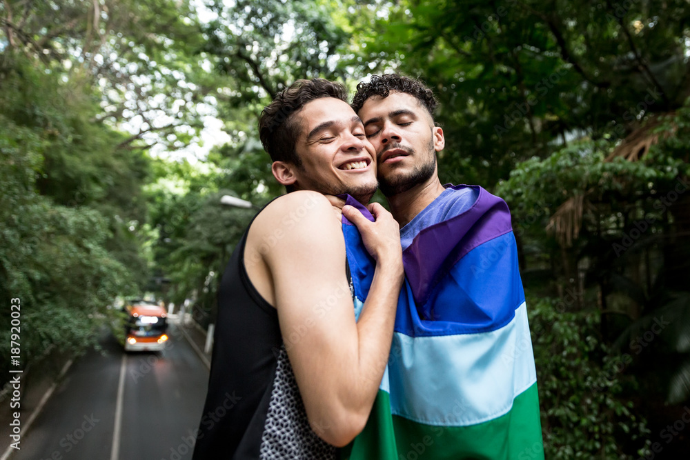 Gay Couple Embracing with Rainbow Flag in the Park Gay Couple Embracing with Rainbow Flag in the Park