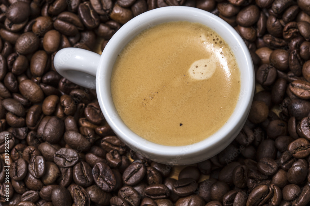 Espresso creamy coffee on a white cup over many brown roasted coffee beans Espresso creamy coffee on a white cup over many brown roasted coffee beans