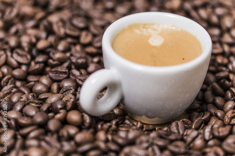 Fototapeta premium Espresso creamy coffee on a white cup over many brown roasted coffee beans