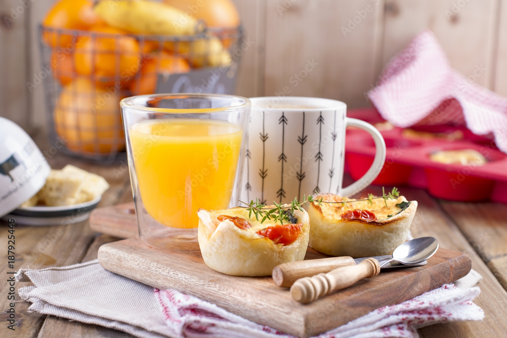 homemade cupcakes with cheese and cherry tomatoes on a wooden board, spoon and knife. table towel in a red cage, a glass of orange juice and fragrant coffee, with space for writing text or advertising
