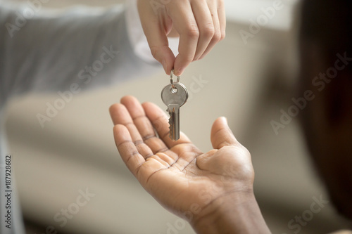 Realtor woman giving african american customer hand taking key, black man buyer house owner purchasing new home, mortgage loan investment contract, buying real estate deal concept, close up view