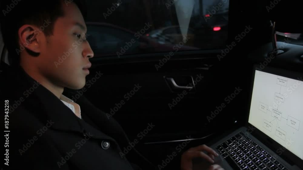 Korean man with laptop is sitting in car. Young male looks attentively at screen of black device on knees and touches touchpad with fingers. Handsome guy dressed in stylish coat and shirt, spends good Korean man with laptop is sitting in car. Young male looks attentively at screen of black device on knees and touches touchpad with fingers. Handsome guy dressed in stylish coat and shirt, spends good