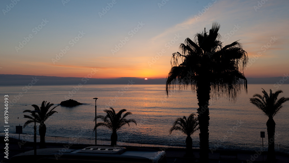 oranger Sonnenaufgang mit Palmen am Meer in Sizilien als Panorama
