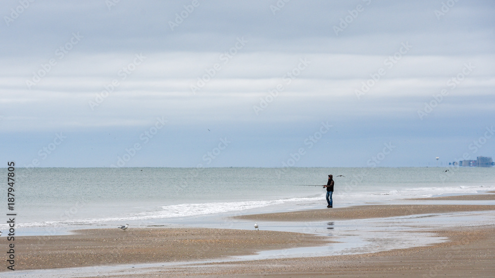 Man fishing on the beach with pole at the ocean with storm clouds in the background