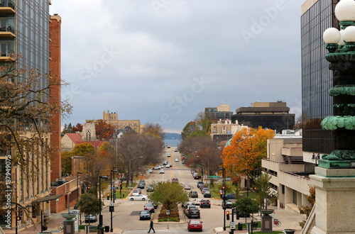 Madison, the capitol of Wisconsin downtown autumn cityscape from the capitol terrace with buildings, street road, traffic cars, traffic lights and lake Monona at the end of street.