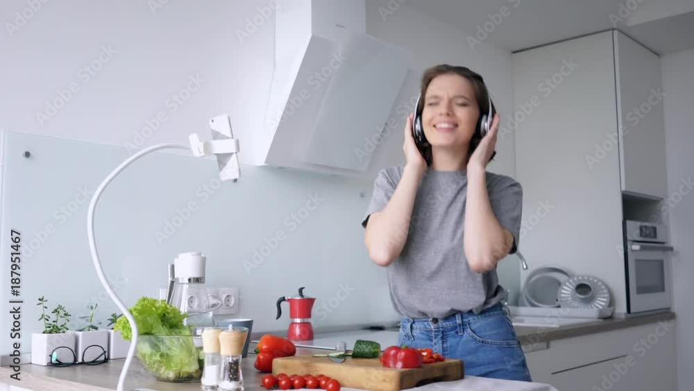 Happy casual woman in headphones cuts vegetables while listening music and dancing on kitchen
Happy casual woman in headphones cuts vegetables while listening music and dancing on kitchen