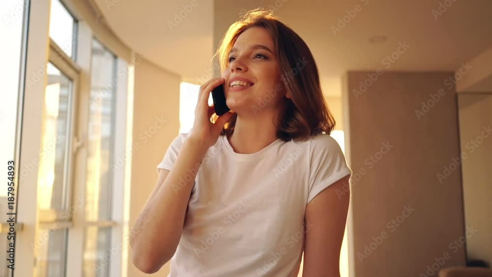 Happy woman sitting on the table and talking by smartphone on kitchen Happy woman sitting on the table and talking by smartphone on kitchen