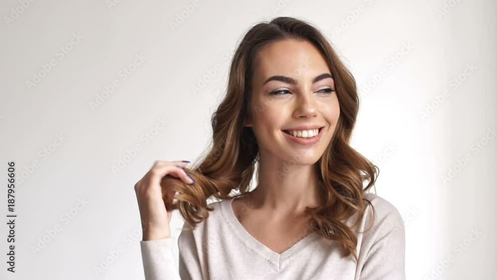 Close up view of sly pensive brunette woman having idea while playing with her hair and looking at the camera over grey background Close up view of sly pensive brunette woman having idea while playing with her hair and looking at the camera over grey background