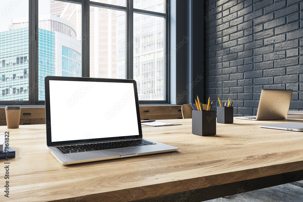 Fototapeta premium White screen laptop in a black brick office