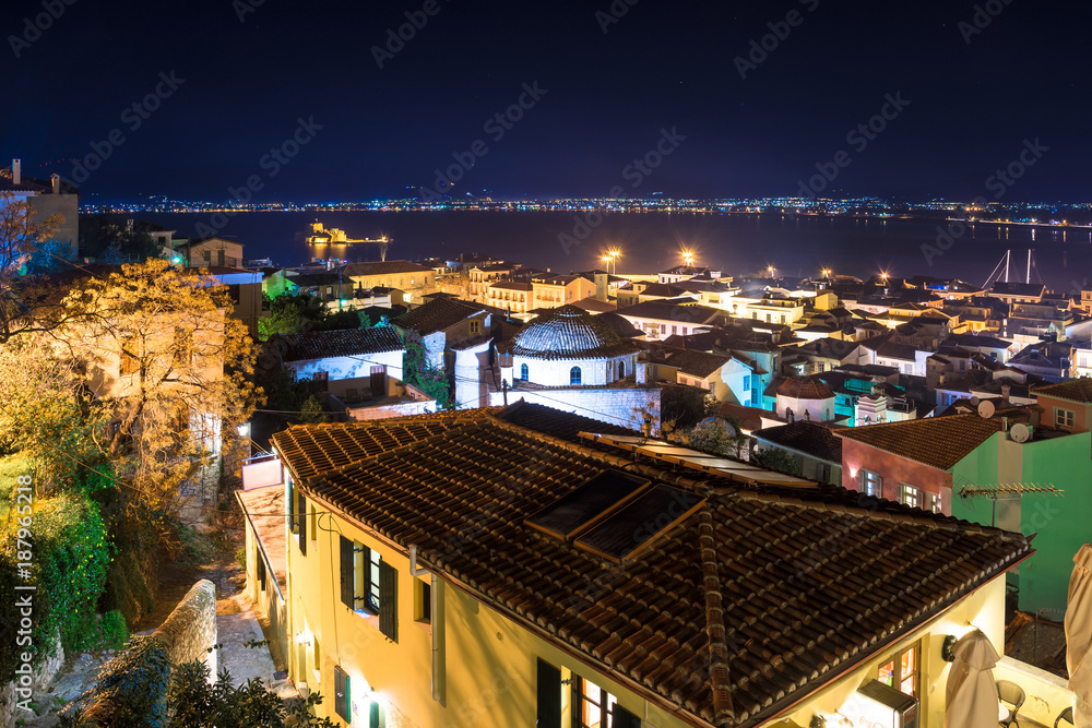 Naklejka premium Illuminated old town of Nafplion in Greece with tiled roofs, small port, bourtzi castle, Palamidi fortress at night.