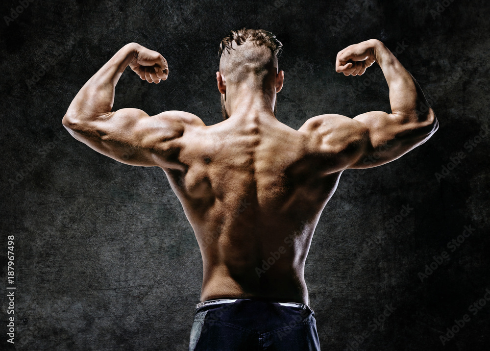 Muscular back of man flexing his arms. Rear view of fitness model with  masculine physique on dark background. Stock Photo