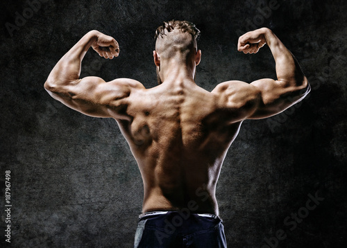 Muscular back of man flexing his arms. Rear view of fitness model with masculine physique on dark background.