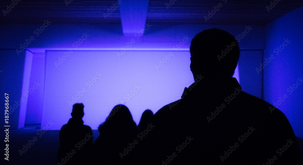 Silhouettes of audience sitting in empty lit theater