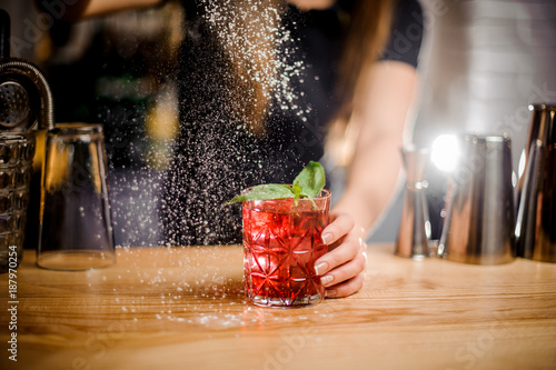 barmaid finishes cocktail preparation by adding a bitter of powdered sugar