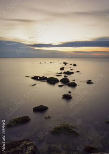 seascape of Silky sea with rocks against a colorful sky at sunrise .