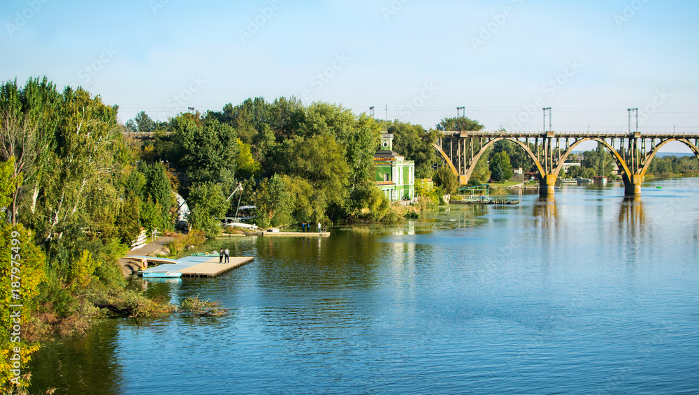 Park Monastery Island, Dnepropetrovsk. Boat mooring and bridge through River Dnepr. Blue water, sky and green trees, early autumn