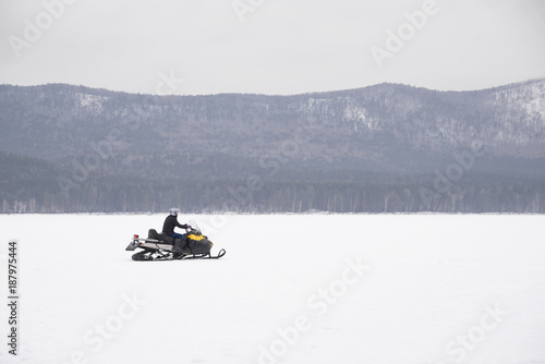 A winter landscape with a snowmobile travelling across frozen ice. mountains in the background