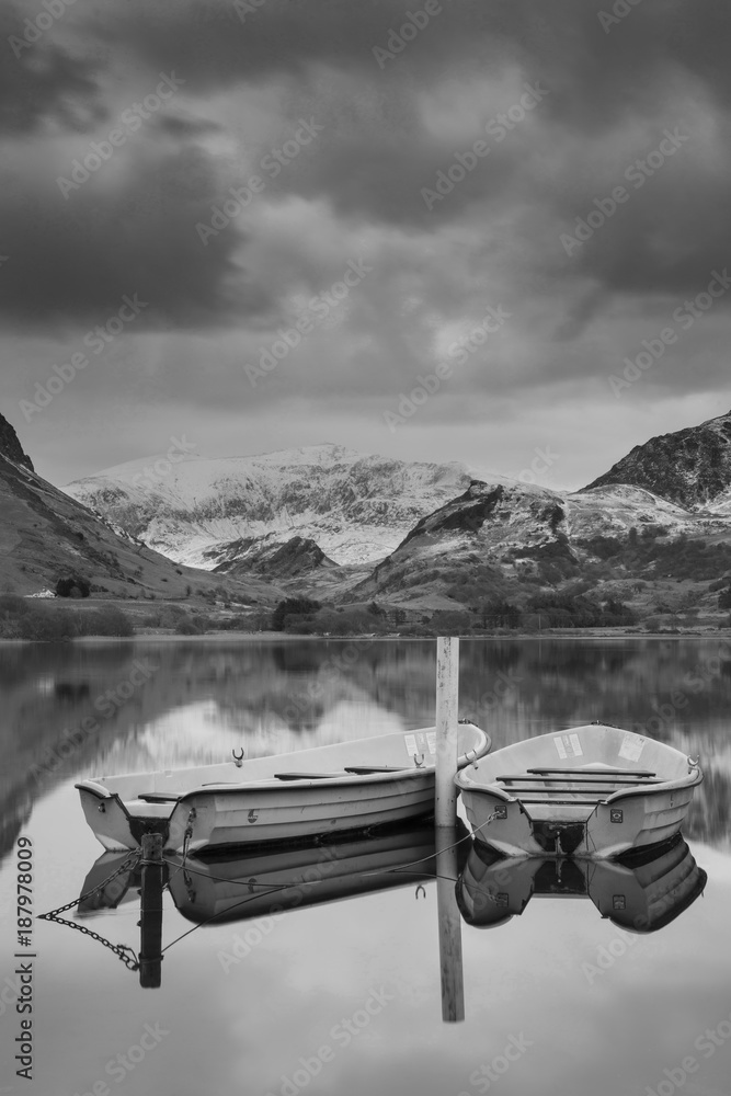 Fototapeta premium Piękny czarny i biały Obraz zimowy krajobraz Llyn Nantlle w Parku Narodowym Snowdonia z ośnieżonymi górami w tle