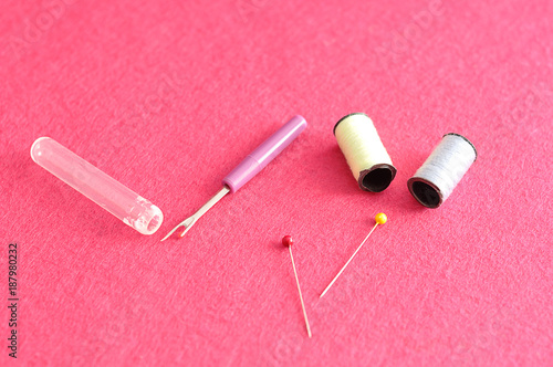 A variety of needlework accessories displayed against a pink background