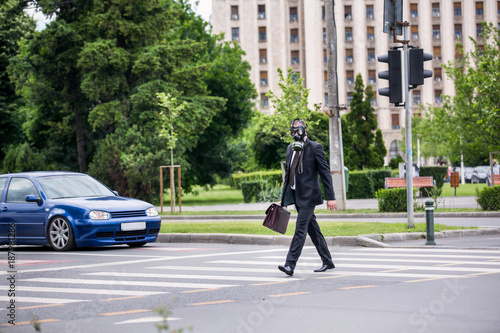 Businessman cross the street outdoor with briefcase wearing a gas mask on the face.