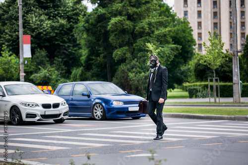 Businessman cross the street outdoor with briefcase wearing a gas mask on the face. © Mindu