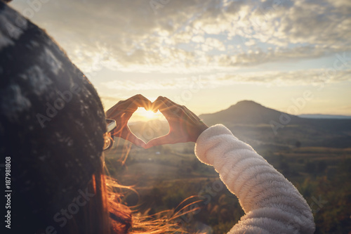 Photo Young woman traveler making heart shape symbol at sunrise
