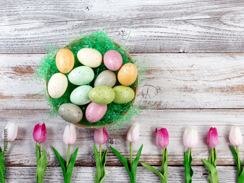 Colorful eggs and tulips for Easter holiday on rustic white wooden background