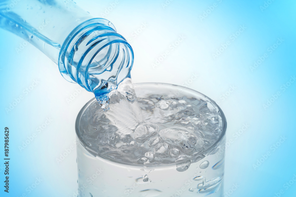 Pouring water from bottle into glass on blue background. Pouring water from bottle into glass on blue background.