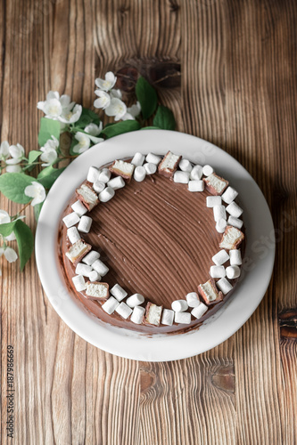 Chocolate cake, decorated with marshmallow, nougat, jasmine flowers on brown wooden table