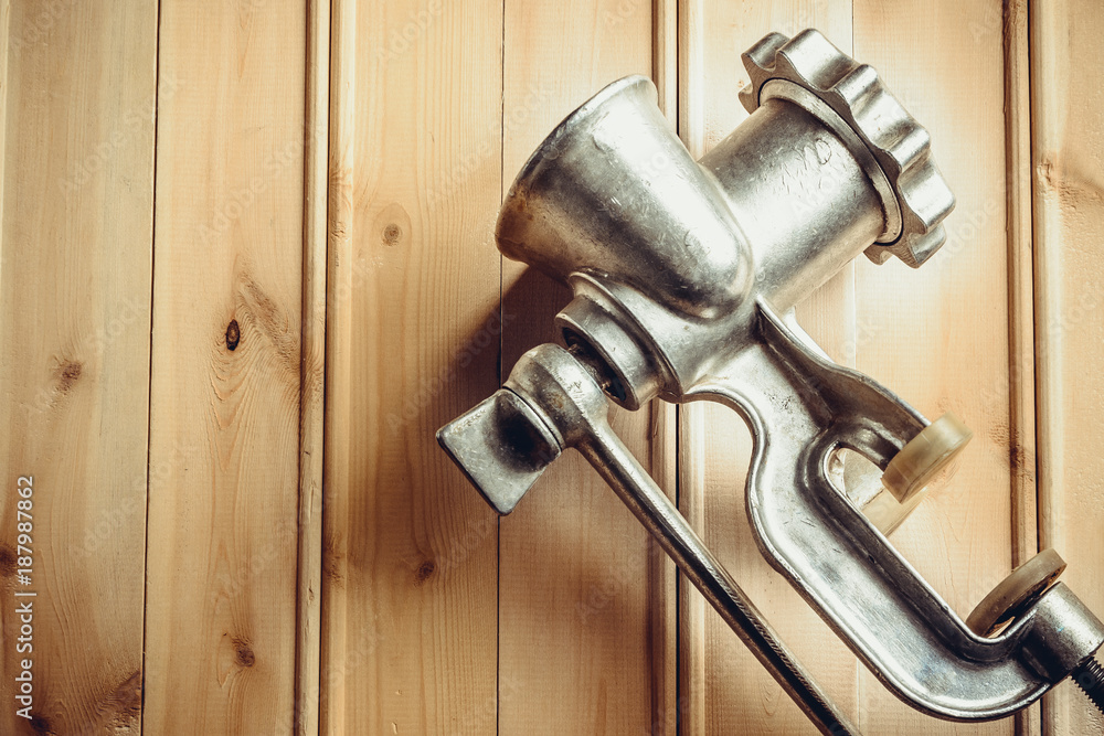 Iron manual meat grinder lying on yellow wooden surface Iron manual meat grinder lying on yellow wooden surface