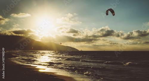 Sunlight sunset on horizon ocean on background seascape atmosphere rays sunrise. Relax view waves sea with kitesurfing on sand beach,  sun light flare nature evening concept, copy space for text.