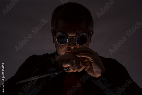 A man is posing with a knife. In safety glasses. Crime.