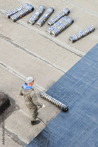 Worker installing roofing felt with heating and melting bitumen roll by torch on flame, high angle view