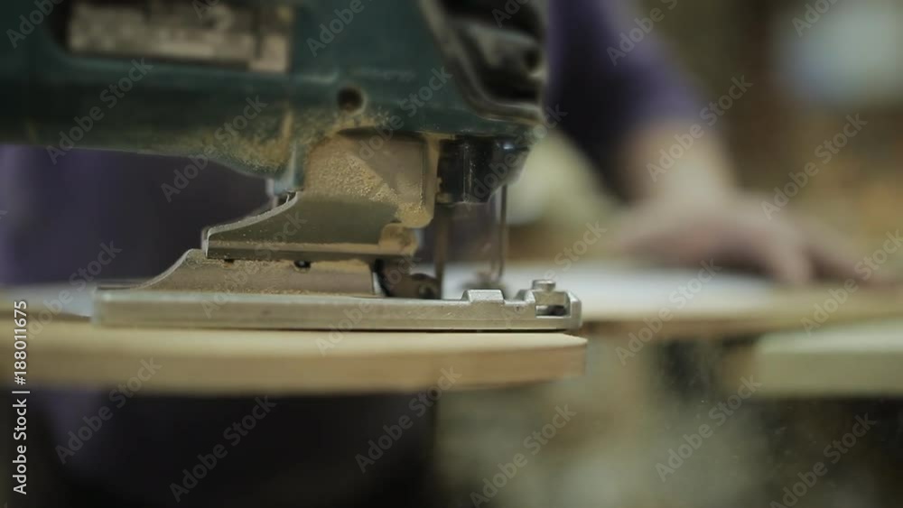 Close-up of electric jigsaw in action. Woman with electric jigsaw. Cutting board. Completion of segments. Manufacturing of furniture Close-up of electric jigsaw in action. Woman with electric jigsaw. Cutting board. Completion of segments. Manufacturing of furniture