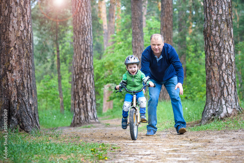 Little kid boy of 3 years and his father in autumn forest with a bicycle. Dad teaching his son. Man happy about success. Child with helmet. Safety, sports, leisure with kids concept.