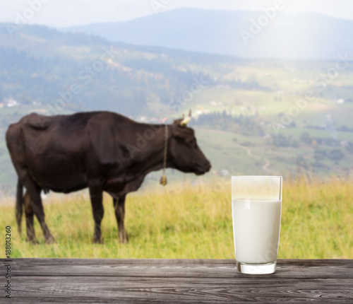 Glass of milk on wooden table on background of cow on mountain p