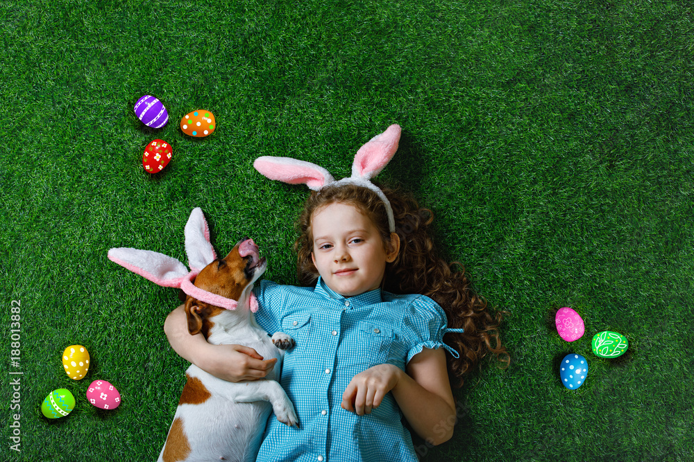 Obraz premium Cute little girl and her dog with rabbit ears lying on green grass
