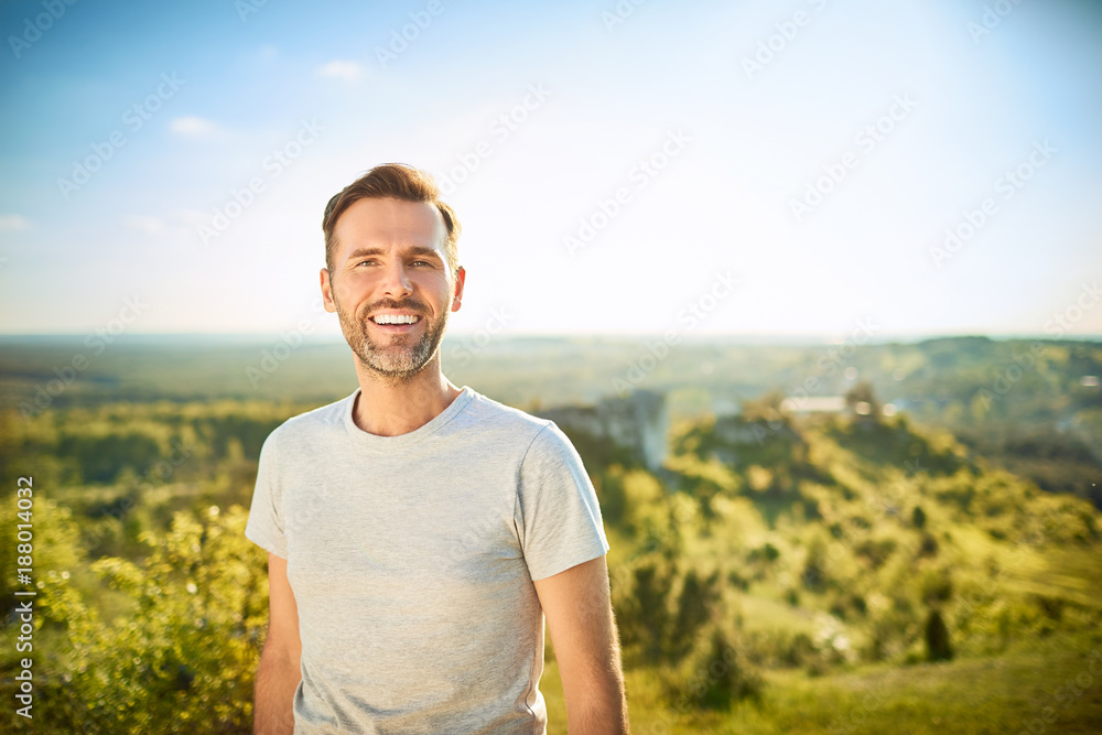 Portrait of man smiling at camera while on trip in the mountains - obrazy, fototapety, plakaty 