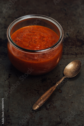 Homemade spicy hot sauce made of dried and roasted habanero, chipotle and jalapeno chiles, tomatoes, onions, garlic and cumin served in glass jar on rustic baking sheet