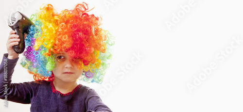 Humorous portrait of cute little girl drying her colorful curly hair with hairdryer. Hair beauty  hair care concept.